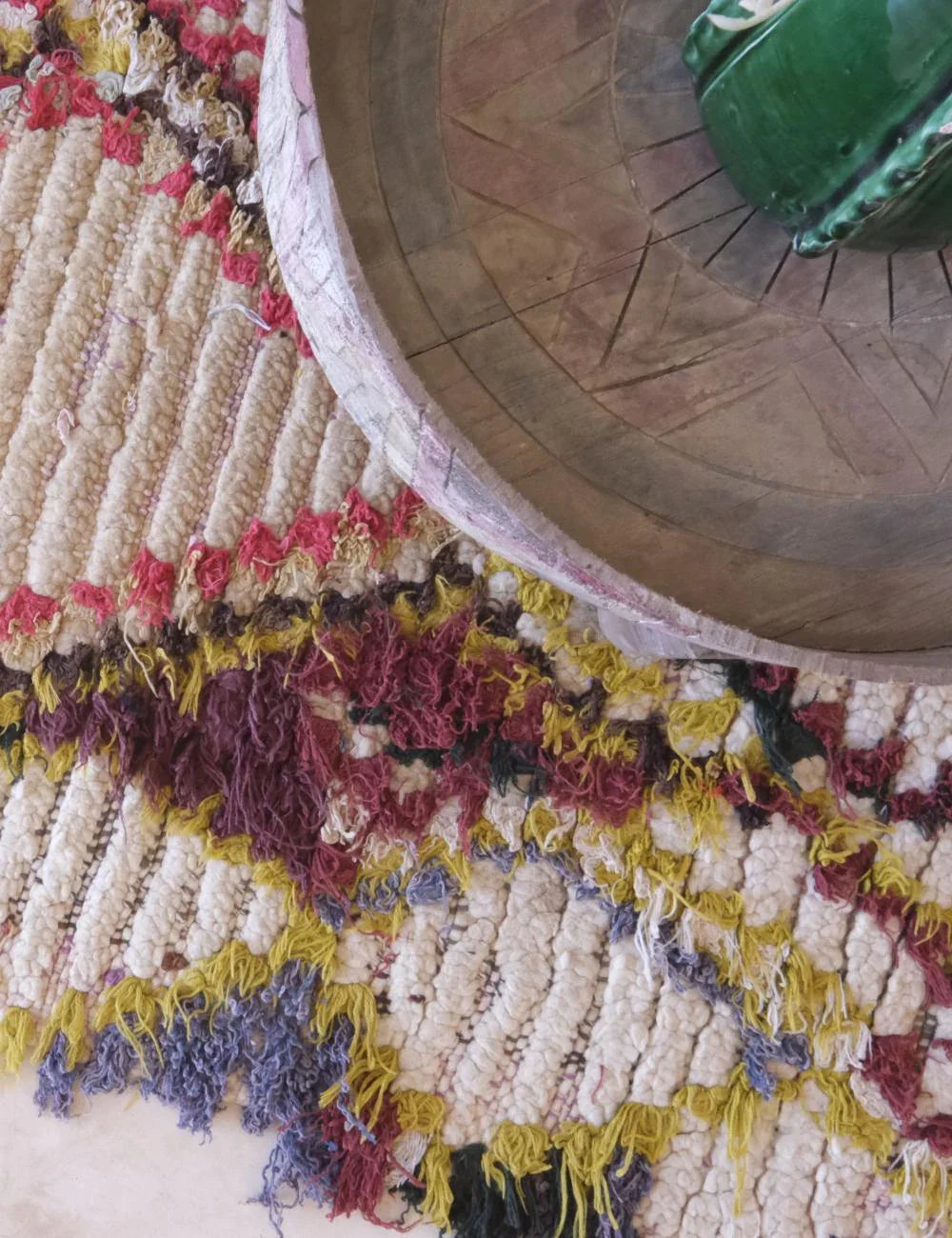 Close-up of a textured rug with a wooden wheel and green object in the background