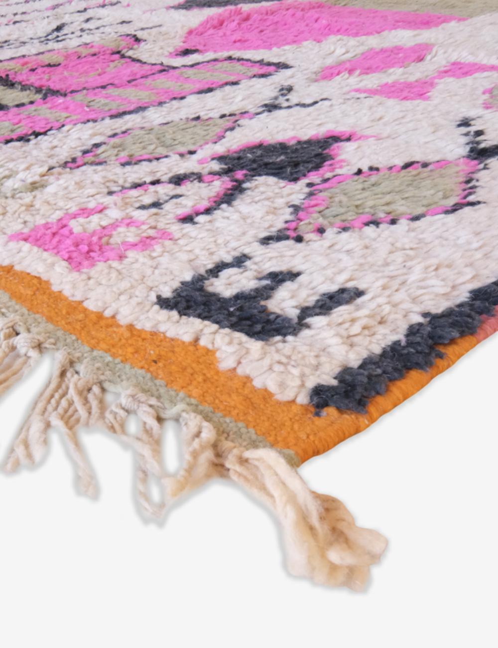Close-up of a colorful woven rug with pink, orange, and gray patterns on a white background.