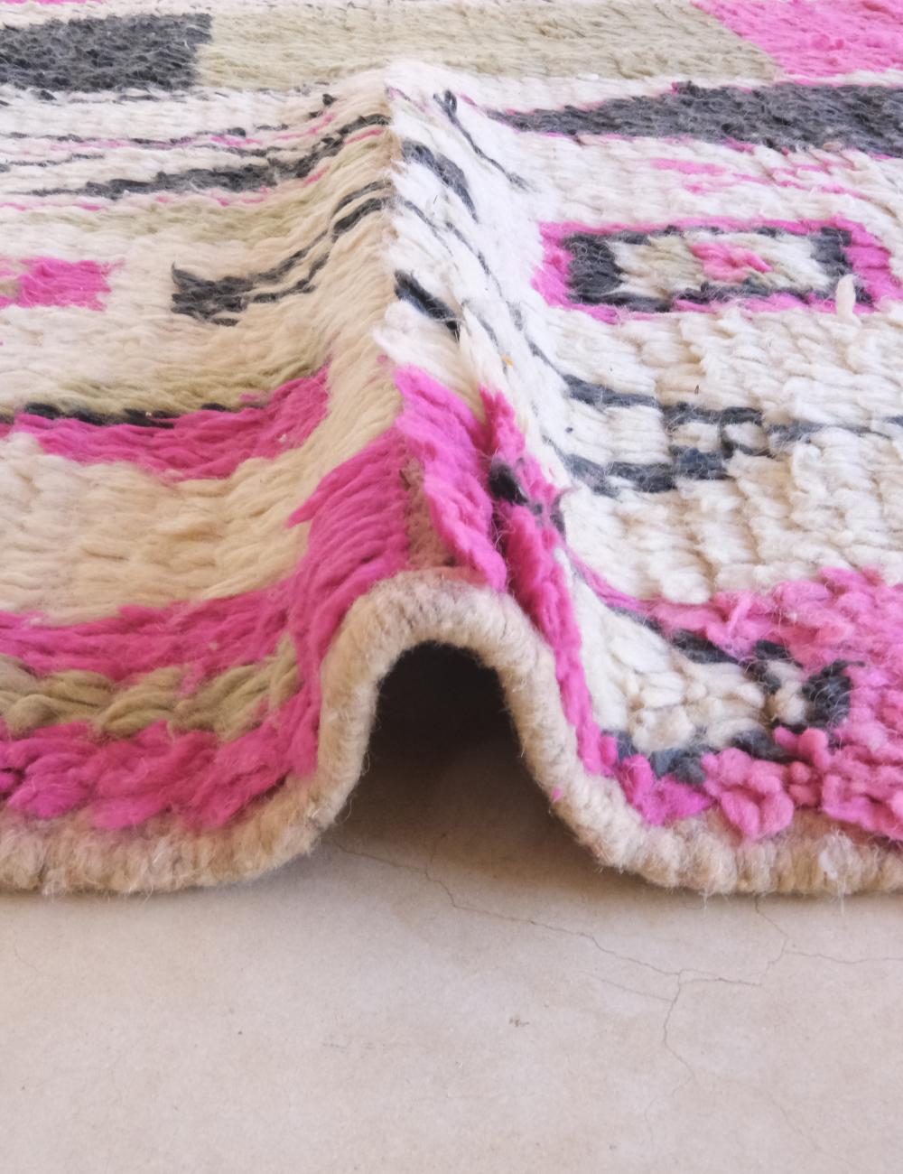 Close-up of a colorful woven rug with pink, beige, and black patterns.