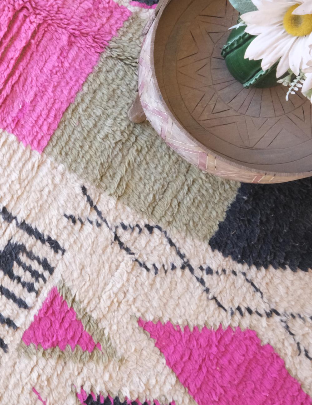 Close-up of a colorful geometric-patterned rug with a decorative bowl and flowers on top.