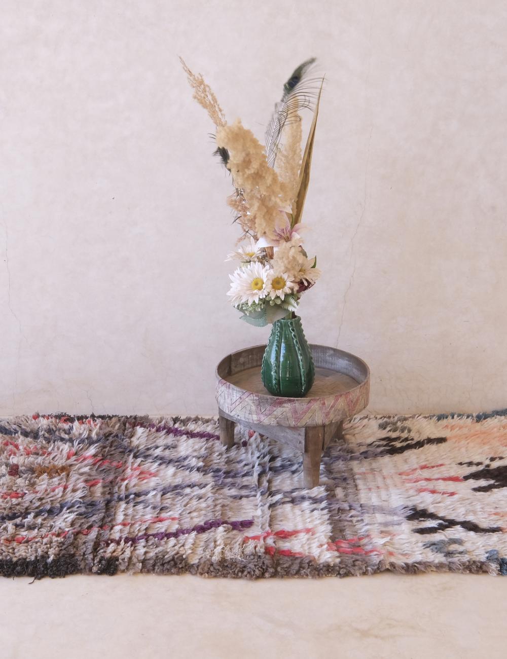 Decorative arrangement with a cactus and dried plants on a small table over a patterned rug.