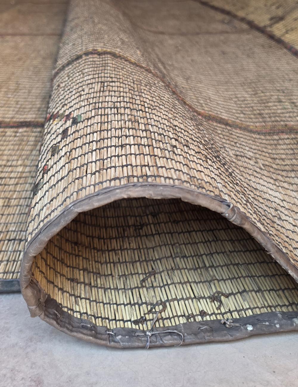 A close-up of a woven natural-fiber mat or rug, shown folded to reveal its texture and underside on a light concrete floor.