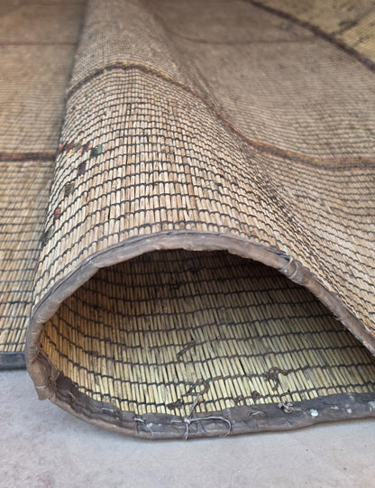 A close-up of a woven natural-fiber mat or rug, shown folded to reveal its texture and underside on a light concrete floor.