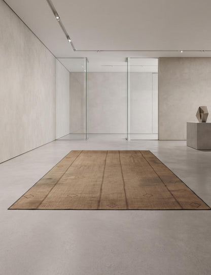 A rectangular vintage-style brown area rug with a rustic, weathered texture, displayed on a minimalist concrete floor in a modern gallery space.