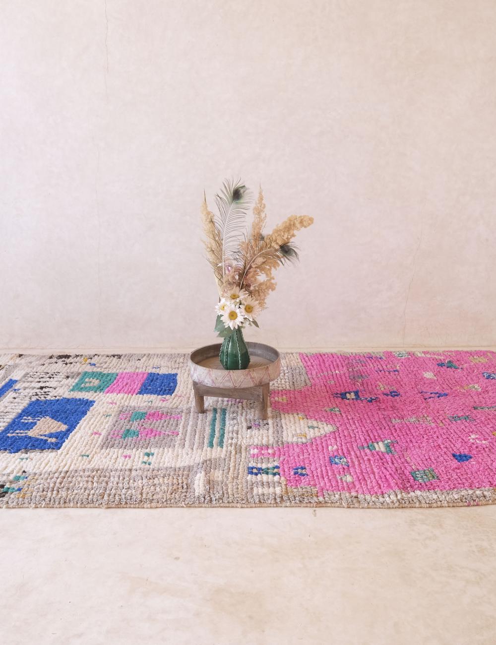Colorful woven rug with a small round table and vase on a light background